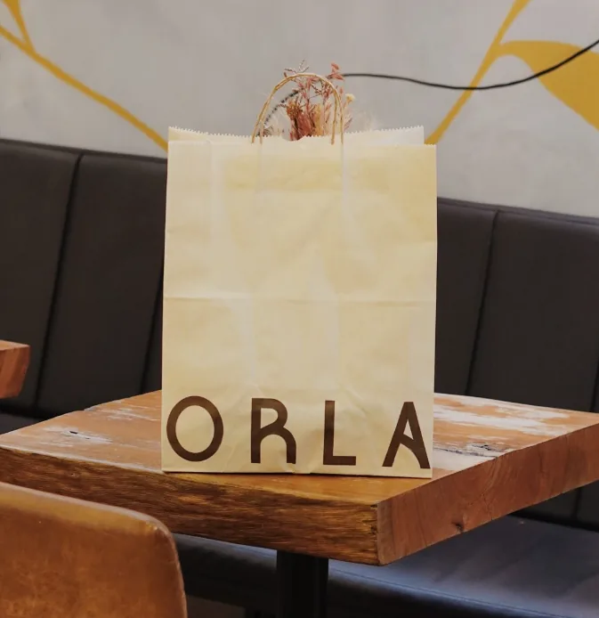 Sacola de papel kraft com a marca ORLA sobre uma mesa de madeira